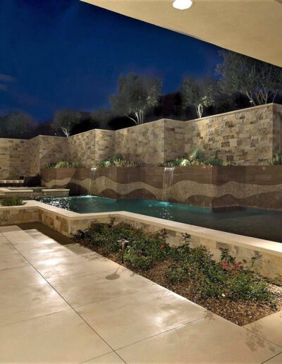 A backyard with a pool and lighting at night.
